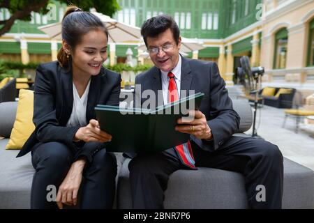 Glücklich reifen Geschäftsmann und junge asiatische Geschäftsfrau das Menü zusammen lesen Stockfoto