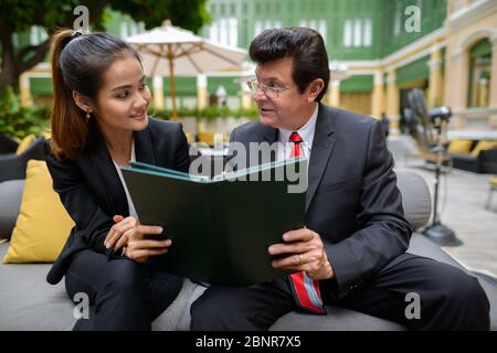 Glücklich reifen Geschäftsmann und junge asiatische Geschäftsfrau das Menü zusammen lesen Stockfoto