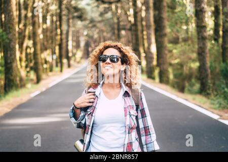 Fröhlicher Reiseflust mit fröhlicher junger kaukasischer Frau, die auf einer Straße mit Wald und schönem Naturholz herumläuft und unterwegs ist Stockfoto