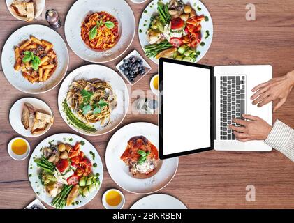 Geschäftsmann arbeitet auf seinem Laptop auf Holztisch mit Tellern von köstlichen italienischen Speisen. Draufsicht Stockfoto