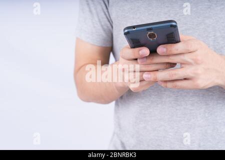 Yong Mann trägt graues T-Shirt Smartphone auf weißem Hintergrund. Technologiekonzept. Stockfoto