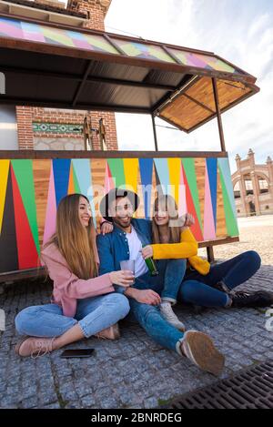 Zwei Mädchen sitzen auf dem Boden neben einem Mann in einem Hut lächelnd und feiern. Bunte und leuchtende Hintergrund mit Platz für Text Stockfoto