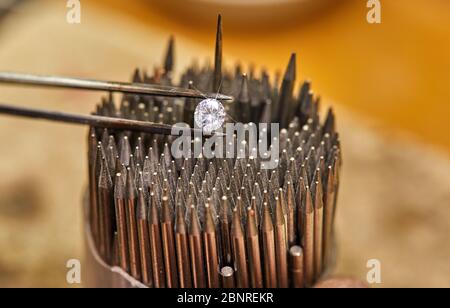 Schmuckherstellung. Der Diamant wird mit einer Pinzette vor dem Hintergrund einer Reihe von Hornhäuten zum Setzen von Steinen gehalten. Stockfoto