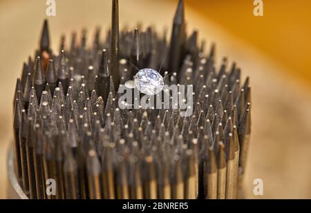 Schmuckherstellung. Der Diamant wird mit einer Pinzette vor dem Hintergrund einer Reihe von Hornhäuten zum Setzen von Steinen gehalten. Stockfoto