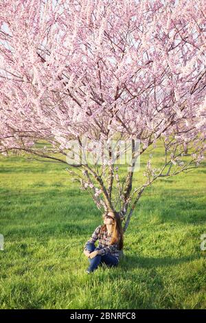 Junge Frau, die unter einem Blütenbaum sitzt. Stockfoto