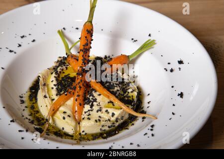 Hummus mit schwarzem Olivenpulver, Olivenöl und Karotten auf einem weißen Porzellanteller serviert.isoliertes Bild Stockfoto