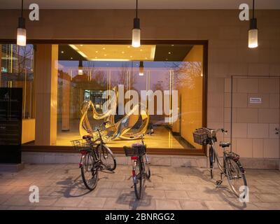 Schaufenster mit Kunstgegenstand und geparkten Fahrrädern in der Abenddämmerung Stockfoto