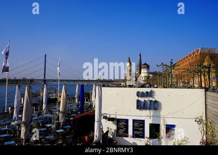 Sonniger Nachmittag an der Rheinpromenade, einer beliebten Touristenattraktion. Café-Außenansicht im Vordergrund, weißer historischer Burgturm im Hintergrund. Stockfoto