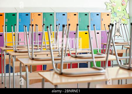 Moderne leere Klassenzimmer mit bunten Spinden und erhöhten Stühlen auf den Tischen - zurück in die Schule Stockfoto