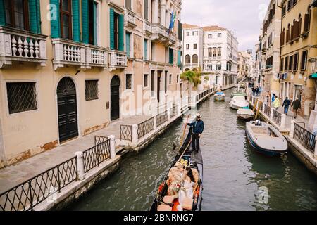 Venedig, Italien - 04. oktober 2019: Italien Hochzeit in Venedig. Ein Gondolier rollt eine Braut und einen Bräutigam in einer klassischen hölzernen Gondel entlang einer engen venezianischen Stockfoto