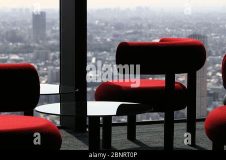 Moderner Cafétisch, der vom Fenster der Lounge eines Wolkenkratzers mit Blick auf die Stadt aufgereiht ist Stockfoto