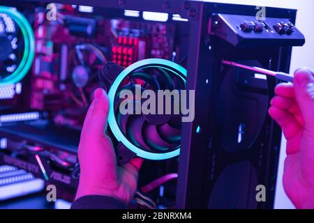 Man setzt modernen Lüfter mit blauem LED-Licht mit Schraubendreher in den Computer Stockfoto