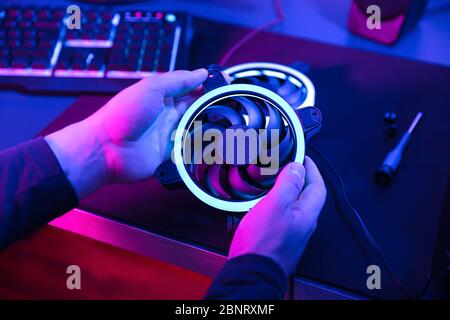 Die Hände des Mannes halten modernen Computerventilator mit blauem Licht mit Tastatur und Lautsprecher im Hintergrund. Stockfoto