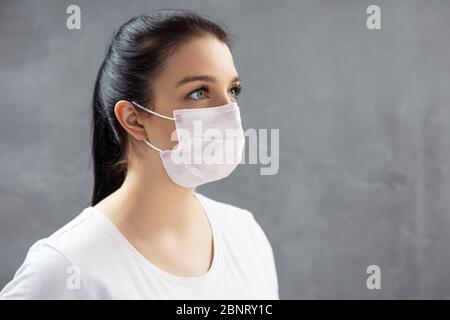 Junge Frau in medizinischer Maske auf betonierten Hintergrund. Stockfoto