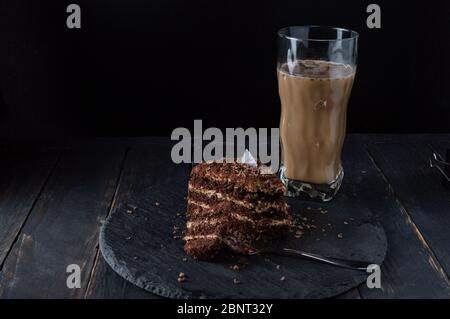 Schokoladenkuchen und Latte beißen. Scheibe Kuchen und Dessertgabel. Latte in einem transparenten Glas. Stockfoto