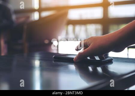 Eine Hand, die das Handy auf dem Tisch packt und abnimmt Stockfoto