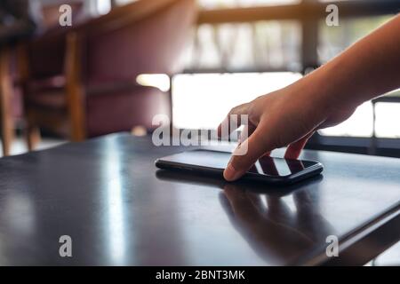 Eine Hand, die das Handy auf dem Tisch packt und abnimmt Stockfoto