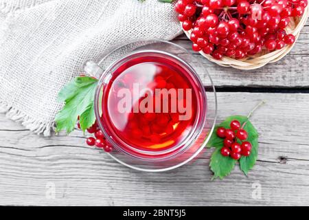 Tee mit Viburnum in einer Glasschale, ein Weidenteller mit Beeren, grünen Blättern und eine Burlap Serviette auf Holzbrett Hintergrund von oben Stockfoto