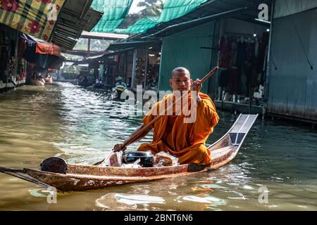 Ratchaburi, Damnoen Saduak / Thailand - 11. Februar 2020: Buddhistischer Mönch, der das Boot auf dem schwimmenden Markt von Damnoen Saduak schlingt. Der Floating-Markt ist am stärksten Stockfoto