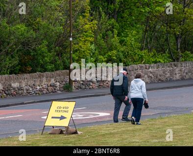 Cockenzie, East Lothian, Schottland, Vereinigtes Königreich. Mai 2020. Covid-19 Teststation: Das ehemalige Kraftwerk Cocenzie, das vom East Lothian Council von Scottish Power gekauft wurde, wird heute als Durchfahrt-Testzentrum COVID-19 eröffnet. Es wird vom Militär (51. Infanterie-Brigade) für Schlüsselarbeiter oder ein Mitglied ihrer Familie mit Symptomen betrieben. Es arbeitet als eigenständige, durchfahrbare Einrichtung - nur nach Vereinbarung - mit Personen, die während der Tests im Fahrzeug als Teil der Test-, Trace-, Isolate-Strategie der schottischen Regierung verbleiben. Ein Paar geht an dem vorübergehenden Schild vorbei Stockfoto