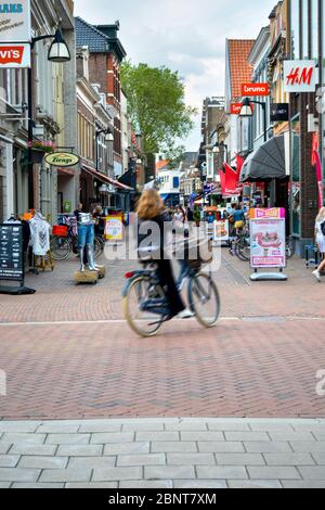 Einkaufsstraße im Zentrum von Meppel. Menschen einkaufen im Hintergrund. Mädchen auf dem Fahrrad geht vorbei. Bewegungsunschärfe. Stockfoto