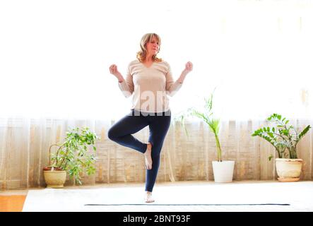 Ganzkörper Erwachsene Frau in Freizeitkleidung Arme heben und Stretching Körper während Yoga auf dem Boden zu Hause Stockfoto