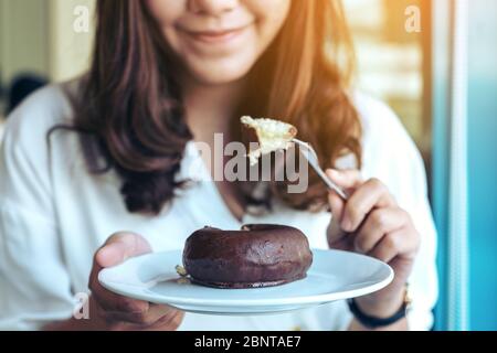 Nahaufnahme Bild einer schönen Frau halten und mit Gabel, um Schokolade Donut in einem weißen Teller essen Stockfoto