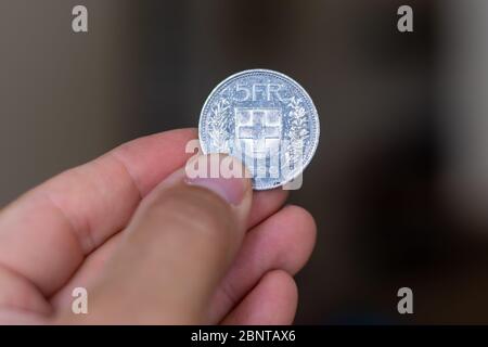 Personen Hand hält eine silberne fünf-Franken-Münze, die Währung der Schweiz - auf einem braunen Hintergrund. Geldwechsel. Stockfoto