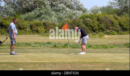 Dorset, Großbritannien. 16. Mai 2020 Golfer spielen den 18-Loch Pitch & Putt Golf in Solent Meads mit Blick auf Christchurch Priory, während die Menschen den Platz und die Sonne am Hengistbury Head Beach genießen, abseits der Menschenmassen in Bournemouth, 5 Meilen westlich der Küste. Dies ist das erste Wochenende nach England lockern Lockdown Maßnahmen & ermöglicht Menschen weiter reisen und Bewegung so viel wie sie wollen. Andrew Fosker / Alamy Live News Stockfoto