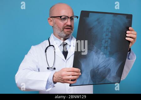 Reifer Arzt in Brille und weiße einheitliche Beobachtung Röntgenbild Wirbelsäule Stockfoto