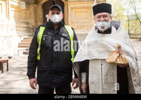 Feier des orthodoxen Osterfestes während der 2020 covid-19 Quarantäne in Kiew orthodoxen Kirche, Priester und Offizier Lächeln, begrüßen Besucher, sorgfältiger Zugang zur Kirche Stockfoto