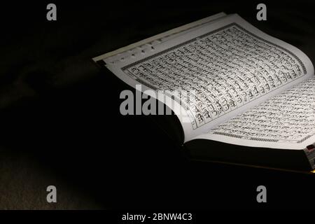 Koranbuch auf braunem Teppich, auf dunklem Hintergrund geöffnet und isoliert Stockfoto