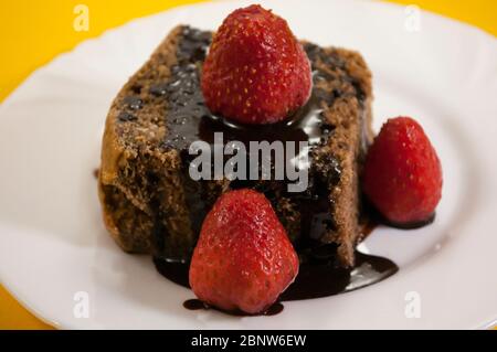 Zwei Schokoladenkuchen mit mehreren Erdbeeren oben in schwarzer Platte auf gelbem Tischhintergrund Stockfoto