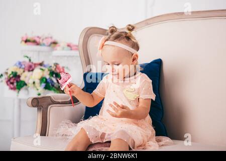 Schönes Mädchen spielt mit Cupcake. Geburtstag Baby. Model, glücklich. Kleines Mädchen mit Kuchen. Kindheit. Kleines Mädchen in einem schönen Kleid isst einen Kuchen Stockfoto