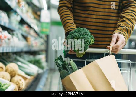 Mann in der Gemüseabteilung im Supermarkt legt Brokkoli in die Papiertüte Stockfoto