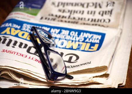 Gefaltete Zeitung mit einem Paar blauer Lesebrille darauf. Kostenlose Informationen und Pressekonzept Stockfoto