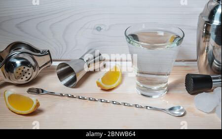 Professionelle Barkeeper-Werkzeuge für die Herstellung von Cocktails auf Holzhintergrund. Eisstücke und Zitrone in der Nähe des Glases Alkohol oder nicht alkoholischen flüssigen Wassers. Stockfoto