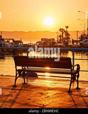 Einsame Bank auf der Promenade am Meer bei Sonnenuntergang Stockfoto