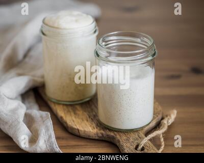 Zwei Glasgläser mit Weizensauerteig-Vorspeisen in verschiedenen Flüssigkeitsstufen. Starter 100 Prozent Hydratation im Hintergrund und Starter mit höherer Hydratation im Vordergrund. Kopierbereich Stockfoto