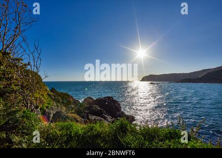 Bild der Bonne Nuit Bay mit der Nordküste, Wellen und Felsen in der Vorgrount und Sonnenaufgang, Sonnenschein, Jersey Channel Islands Stockfoto