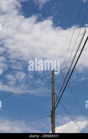 Strompol zur Unterstützung elektrischer Stromleitungen, die in drei Richtungen verlaufen, isoliert gegen einen blauen Himmel mit Wolken, vertikaler Aspekt Stockfoto