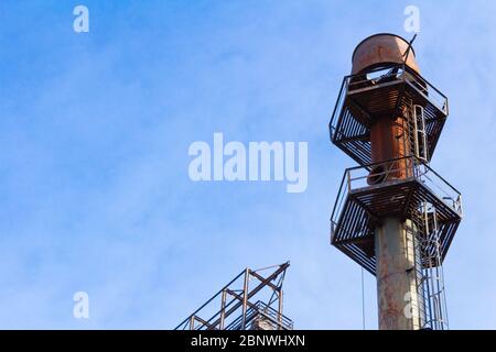 Sechseckige Plattformen, die durch Leitern auf einem riesigen Schornstein verbunden sind, verfallende industrielle Komplex, blauer Himmel kopieren Raum, horizontaler Aspekt Stockfoto