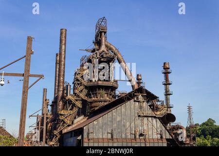 Massive Industrieanlage, verlassene und verwitterte Öfen und Rauchschornsteine vor einem tiefen blauen Himmel, horizontaler Aspekt Stockfoto