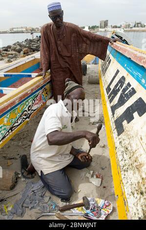 Männer reparieren ein traditionelles Pirogue-Fischerboot am Strand von Soumbedioune, Dakar, Senegal. Stockfoto