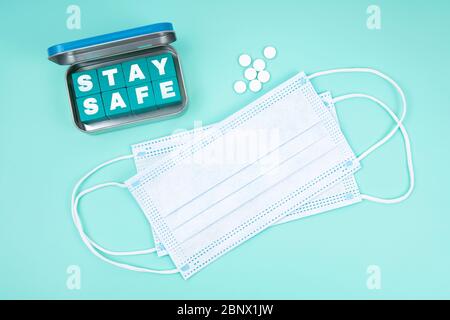 Einweg-Gesichtsmasken, Pillen und eine Stahlbox mit Holzbuchstabenwürfeln Schreibweise BLEIBEN SIE SICHERER Text, der eine Nachricht übermittelt, um zu kümmern und Regeln zu beachten. Stockfoto