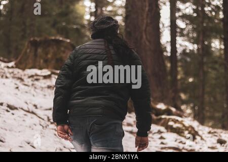 Mann mit Stillstand Haar geht in einem verschneiten Wald, erkundet die Umgebung, Blick von hinten, 5K Stockfoto