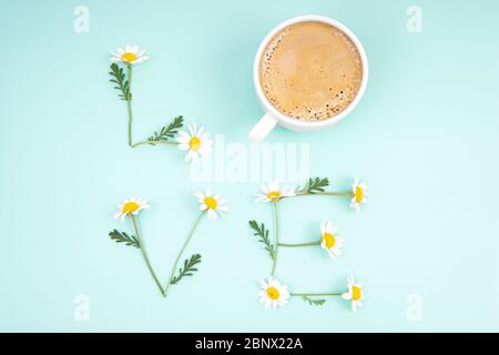 Kreative romantische Komposition, die das Wort LIEBE der Kamille Blumen und eine Kaffeetasse auf hellblauem Hintergrund. Lebendige und zarte frische Tasse Liebe Stockfoto