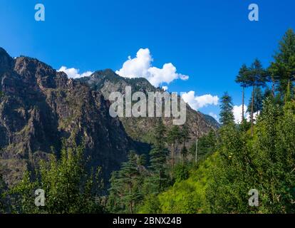 Landschaft aus Bergen und grünen Bäumen an einem hellen blauen schönen sonnigen Tag, weiße Wolken schweben über den Hügeln, 5K Stockfoto