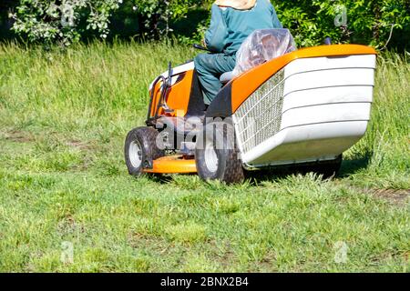 Der Gärtner mäht an einem klaren sonnigen Tag grünes Gras auf dem Rasen mit einem professionellen Traktor-Rasenmäher, Platz kopieren. Stockfoto