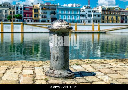 Selektiver Fokus auf einen Poller mit Triana-Distrikt im Hintergrund während der Coronavirus-Pandemie in Sevilla. Guadalquivir Fluss. Stockfoto